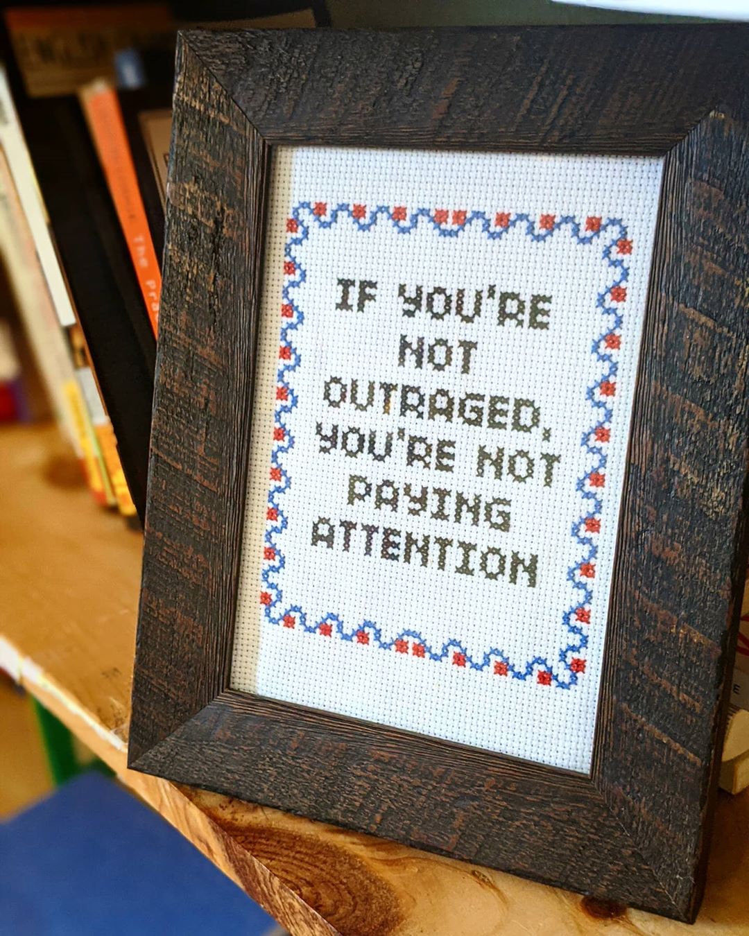 A framed embroidery of the quote 'If you're not outraged, you’re not paying attention'